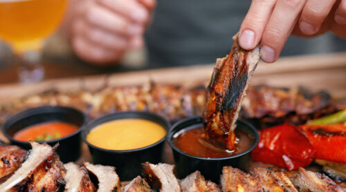 A diner dips ribs in BBQ sauce.