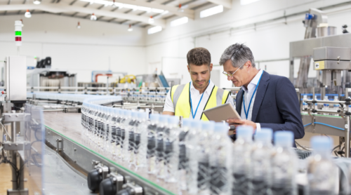 Two workers examine a production line up close.