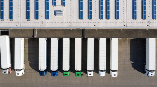 Delivery trucks lined up outside a distribution center viewed from above.