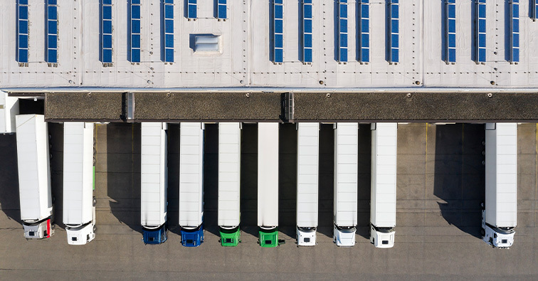 Delivery trucks lined up outside a distribution center viewed from above.