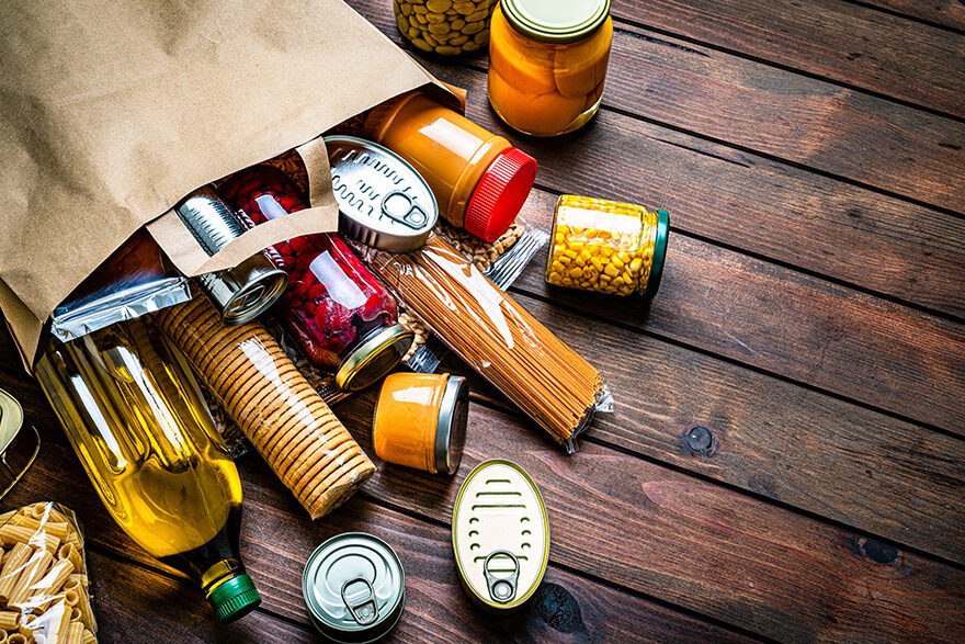 A bag of groceries is splayed across a brown wooden table.