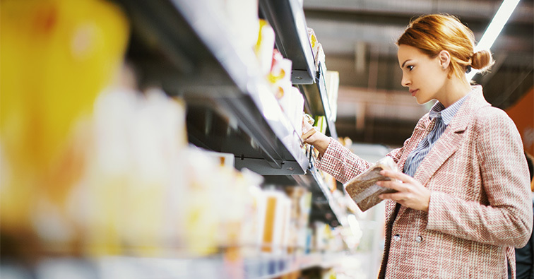 A women examines nutrition labels in a grocery store aisle.