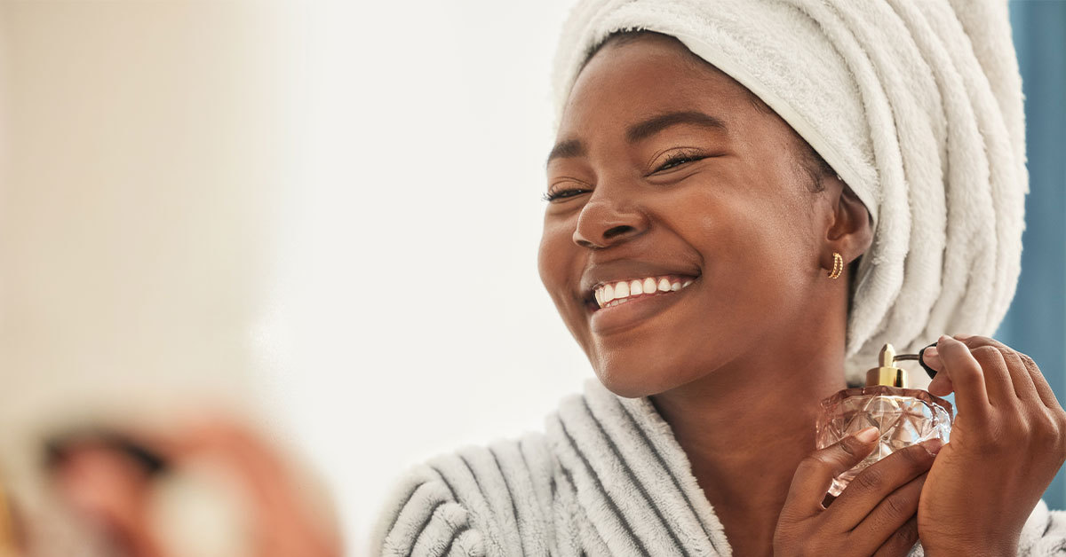 A smiling women in a soft robe applies fine perfume.