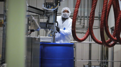 A lab worker in a white coat prepares a chemical formulation.