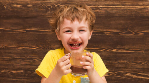 Smiling young boy enjoys a glass mug of delicious chocolate milk.