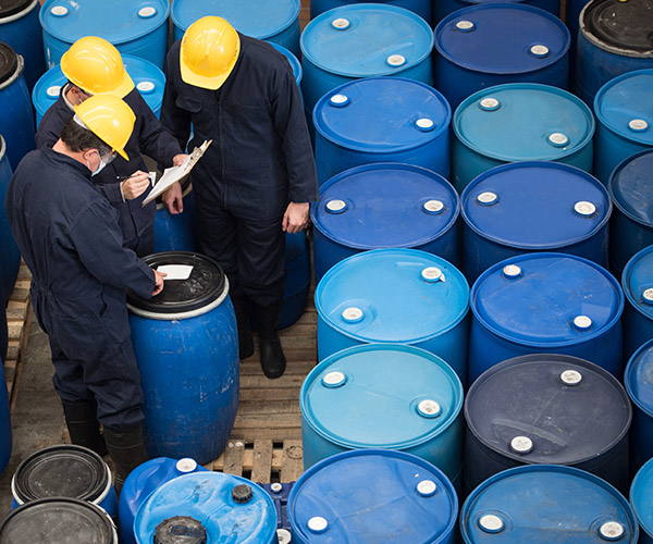 Men in hard hats studying clipboard, surrounded by blue industrial drums.