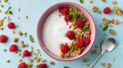 A bowl of yogurt with fresh raspberries and granola.