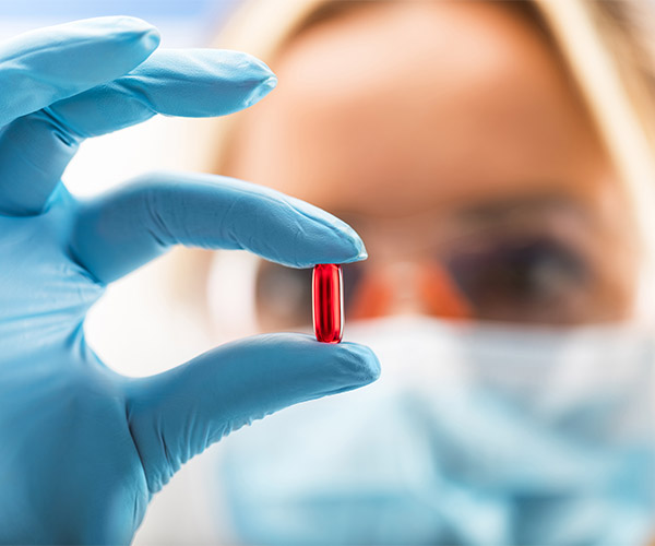 Woman wearing gloves, holding up a red gel pill.