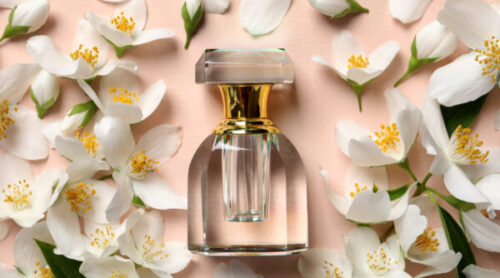 Bottle of luxury perfume and fresh jasmine flowers on beige background, flat lay