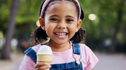 A young girls smiles with a half-eaten ice cream cone.