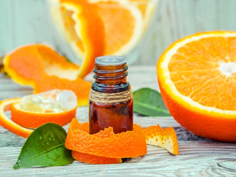 A vial of citrus fragrance surrounded by sliced oranges.
