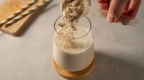 A person adds plant-based protein powder to a glass of non-dairy milk.