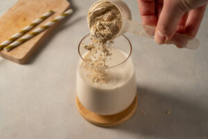 A person adds plant-based protein powder to a glass of non-dairy milk.