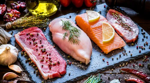 Several cuts of uncooked meat sit on a blue cutting board.