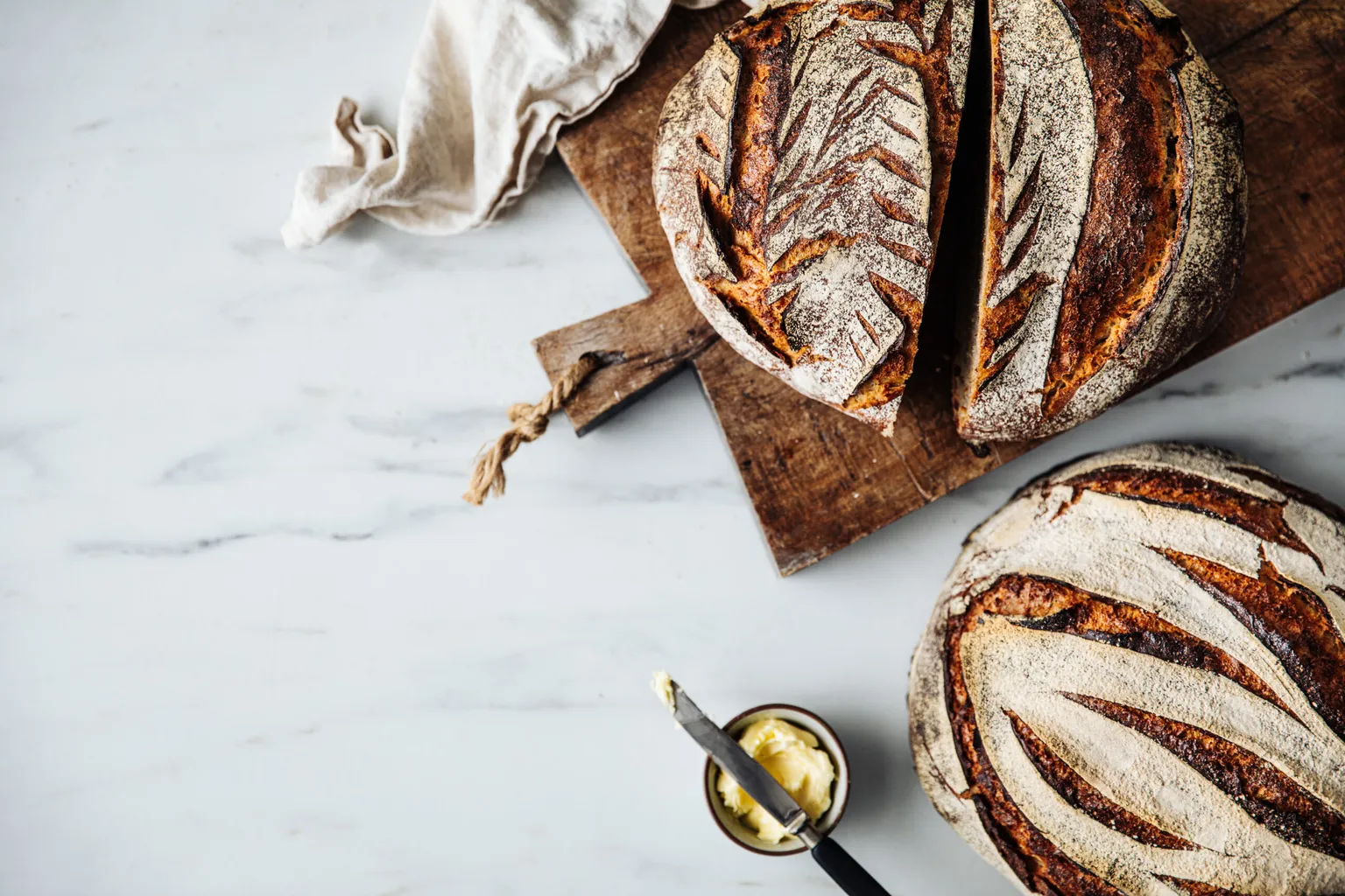 Directly above view of fresh sourdough bread on cutting board. Close-up of butter and knife on marble counter. It is made of wheat and rye.